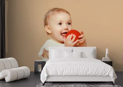 Cute baby holding red apple fruit sitting on the floor on brown studio background Wall mural