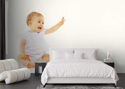 Cute baby looking up sitting on the floor greeting waving his hand on white background, banner blank copy space for advertising text Wall mural