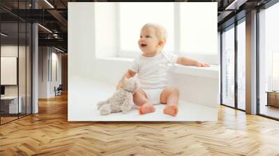 cute smiling baby with teddy bear toy sitting at home in white r Wall mural