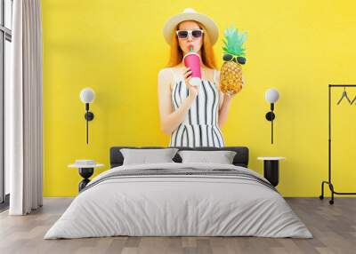 Fashion pretty woman with a pineapple, cup of juice in white striped pants, round hat on yellow background Wall mural