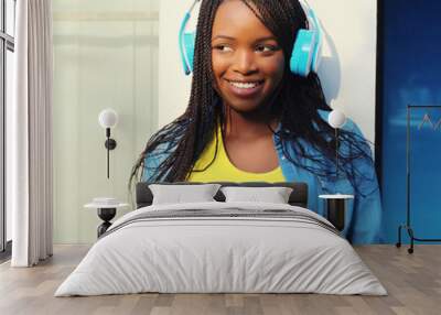 Happy african woman listening to music with smartphone, black girl smiles in headphones holds phone Wall mural