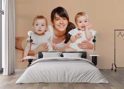 Happy cheerful smiling young mother holding baby on brown background Wall mural