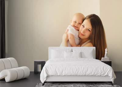 Happy smiling young mother playing with baby in white room at home Wall mural