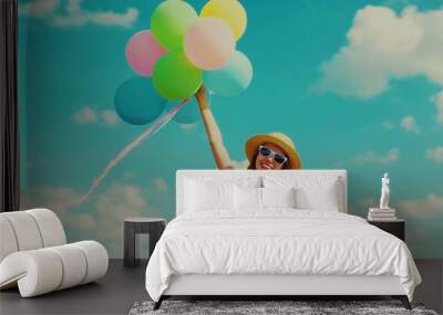 Happy smiling young woman with bunch of colorful balloons wearing a summer straw hat on the field on a blue sky background Wall mural