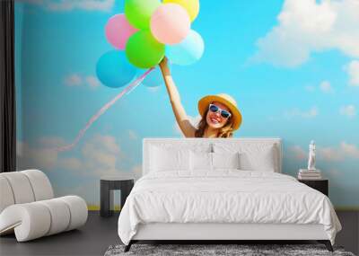 Happy young smiling woman holds an air colorful balloons at summer day over meadow blue sky Wall mural