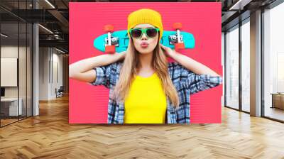 Portrait cool woman with skateboard wearing colorful yellow hat on pink background Wall mural