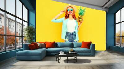 Portrait happy smiling woman with pineapple having fun in summer straw hat, sunglasses, shorts on colorful yellow background Wall mural