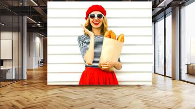 Portrait happy surprised laughing woman wearing red beret holding paper bag with long white bread baguette on white wall background Wall mural