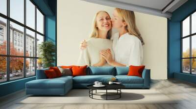 Portrait of adult daughter kissing her happy smiling caucasian middle aged mother on studio background Wall mural