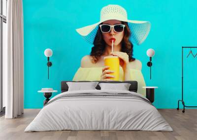 Portrait of beautiful young woman drinking a fresh juice wearing a summer hat on blue background Wall mural