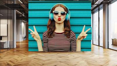 Portrait of cheerful young woman with headphones listening to music on a colorful blue background Wall mural