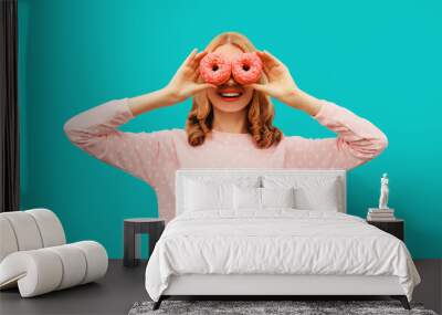 Portrait of happy funny laughing woman covering her eyes looking for something looking through donuts as binoculars having fun on blue background Wall mural