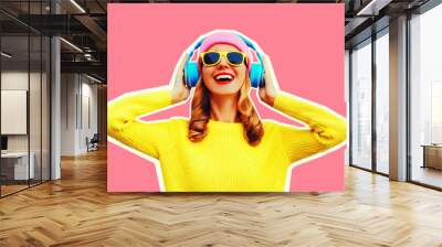 Portrait of happy smiling young woman in headphones listening to music wearing colorful yellow sweater on pink background, magazine style Wall mural