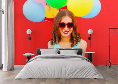 Portrait of happy smiling young woman with gift box and colorful balloons on red background Wall mural