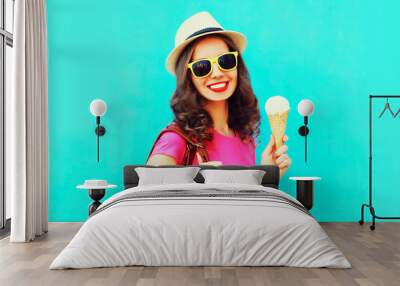 Portrait of happy smiling young woman with ice cream wearing summer straw hat on blue background Wall mural