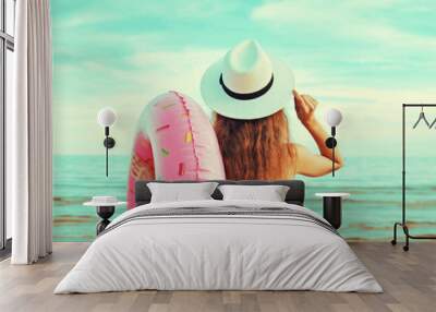 Portrait of happy smiling young woman with inflatable ring wearing straw hat on beach on sea background Wall mural