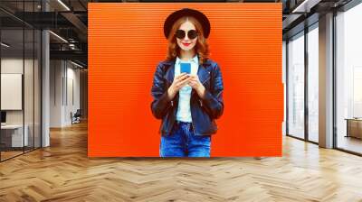 Portrait of stylish smiling woman with smartphone wearing black round hat, leather biker rock jacket on red background, blank copy space for advertising text Wall mural