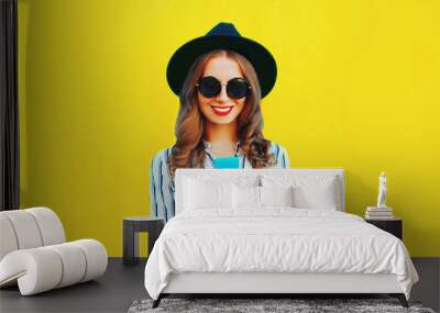 Portrait of stylish woman with smartphone wearing black round hat, white striped shirt on yellow background Wall mural