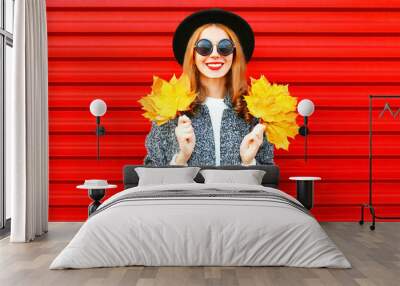 Pretty autumn smiling cool girl with yellow maple leaves on a red background Wall mural