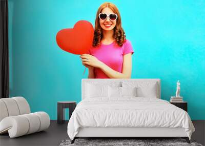 smiling woman with a red air balloon in the shape of a heart on blue background Wall mural