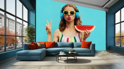 Summer fashion portrait of young woman in headphones listening to music with juicy slice of watermelon, female model blowing her lips posing on a colorful blue background Wall mural