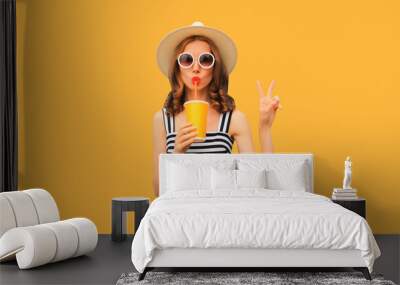 Summer portrait of beautiful young woman drinking fresh juice wearing straw round hat, striped dress on orange background Wall mural