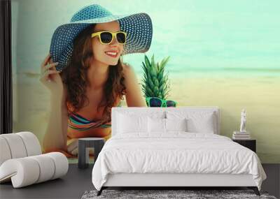 Summer portrait of happy smiling young woman lying on the beach with funny pineapple wearing straw hat Wall mural