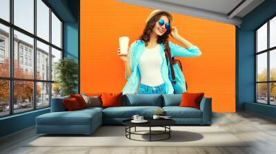 Summer portrait of happy smiling young woman with cup of coffee wearing straw hat, backpack and shirt on orange background, blank copy space for advertising text Wall mural