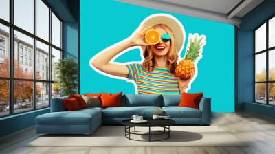 Summer portrait of happy smiling young woman with pineapple and slice of orange, fresh tropical juicy fruits, wearing straw hat, sunglasses on blue background Wall mural