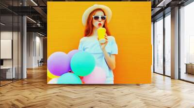 Summer portrait of happy woman drinking fresh juice with colorful balloons having fun wearing straw hat on orange background, blank copy space for advertising text Wall mural