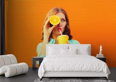 Summer portrait of happy young woman drinking fresh juice with slice of orange fruits and looking away on background Wall mural