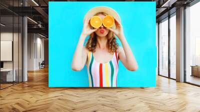 Summer portrait woman holding in her hands two slices of orange fruit hiding her eyes in straw hat on colorful blue background Wall mural