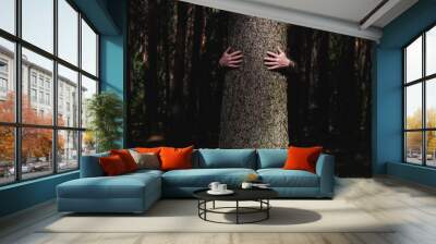 Human hug a tree in the dramatic light at the forest. Nature love. Earth day concept. Male hands touch old tree Wall mural