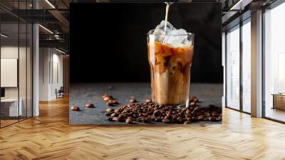 ice coffee in a tall glass with cream poured over ice cubes and beans on a dark concrete table Wall mural