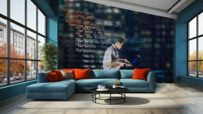 Young male student in school uniform sitting on a floor of an office while coding for a website, view from outdoor behind the office glass with city light reflections and computer codes projecting. Wall mural