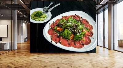 meat carpaccio on white plate on black wooden background Wall mural