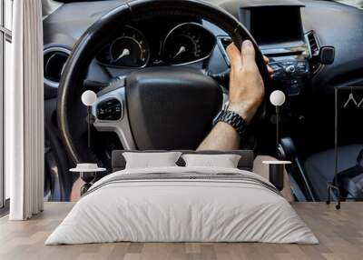 A man's hand is holding the steering wheel of a car and trying to turn the steering wheel. Wall mural