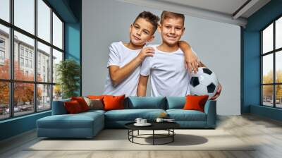 active boys with soccer ball in hands, young caucasian teenagers posing, hugging each other, engaged in sport, play in the same team Wall mural