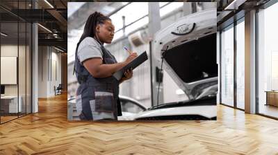 African american technician female concentrated to check list for maintenance in car garage service, wearing overalls uniform, looking focused while writing in documents tablet. side view Wall mural