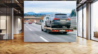 Tow truck with car on warranty in road. Trailer and crash auto delivery. Vehicles hauler on driveway. European transport logistics. Heavy haul trailer with driver on highway. Wall mural