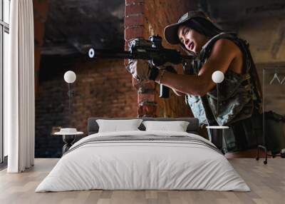 Beautiful and attractive female army soldier posing with gun rifle weapon. Woman with weapon. Firearm shooting range gun shooting training in abandoned building. Caucasian lady is fighting with enemy Wall mural