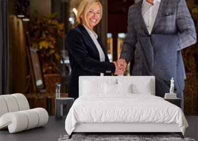 business partners shaking hands and smiling at camera, wearing formal suits, at business trip in hotel, with yellow suitcase, in the hall Wall mural