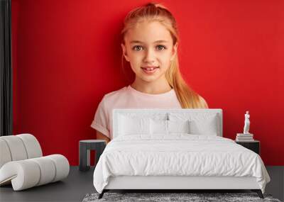 calm diligent child girl with long hair isolated on red background in studio, she looks at camera smiling Wall mural