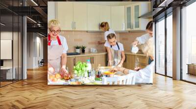 Caucasian Grandmother and granddaughters cooking in bright kitchen. Family enjoy cooking, wearing apron, adding ingredients to pizza, at home in holiday, preparing to have dinner together. side view Wall mural