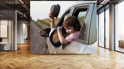 A fragment of a car with a happy child in the window. A motorist and a girl wave straw hats as they approach the seashore. Selective focus. Wall mural