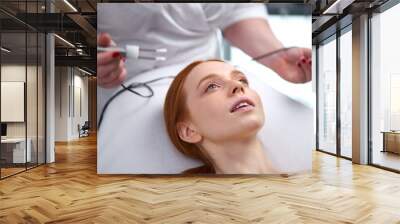 facial skin rejuvenation by microcurrent therapy in cosmetology salon, using special device to perform a facial rejuvenation procedure for attractive caucasian young female Wall mural