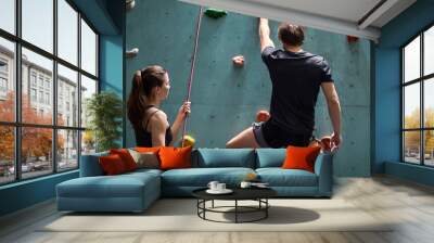 Female instructor giving instructions to man on wall climbing. man learning the art of rock climbing at an indoor climbing centre, wearing safety equipment Wall mural