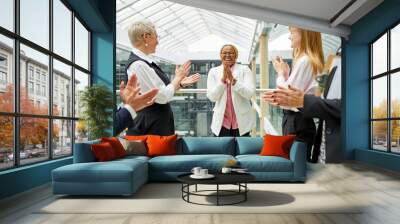 friendly caucasian colleagues congratulating african co-worker with a good result at work, clapping hands, woman is happy in the center Wall mural