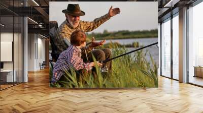 Grandfather and kid boy together fishing in the evening at sunset time in summer day on river in countryside, side view on caucasian multi-generation family, elderly man teach child boy to fish Wall mural