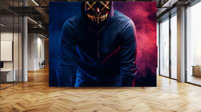 hacker man involved in criminal wearing scary mask and pullover, in a hood. man look at camera, want to hack system of laptop, to take necessary information from it. isolated smoky neon space Wall mural